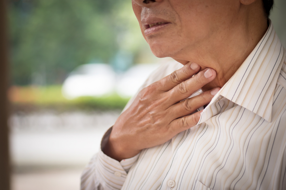 Elderly person touching their throat after feeling pain