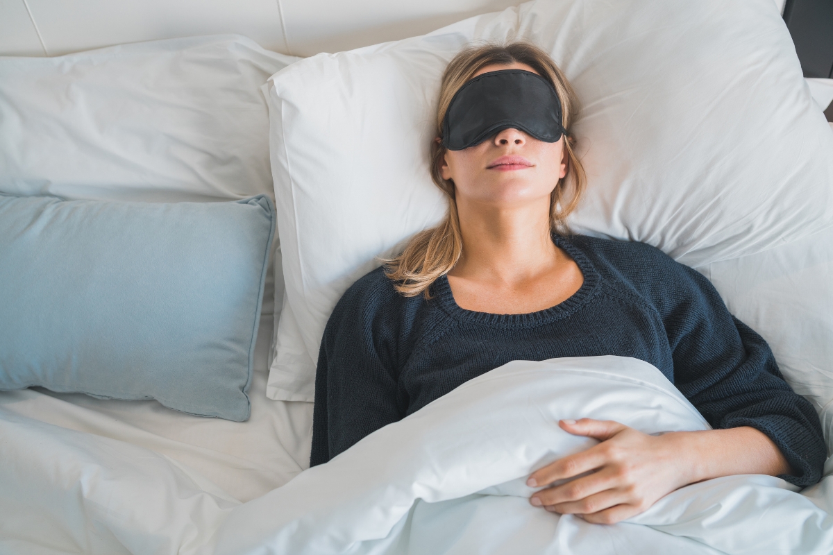 Woman sleeping in bed with an eye mask, representing healthy sleep and its connection to oral health