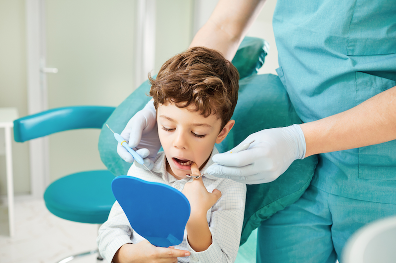 Child receiving a dental exam while looking in a mirror during a pediatric visit focused on jaw alignment and breathing development