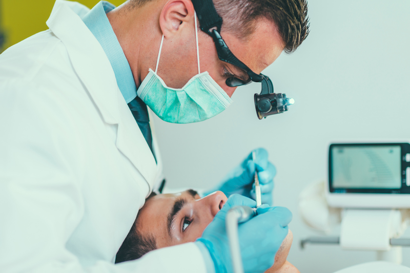 Dentist examining a patient’s tooth during a procedure to determine whether a root canal or tooth extraction is the best treatment option